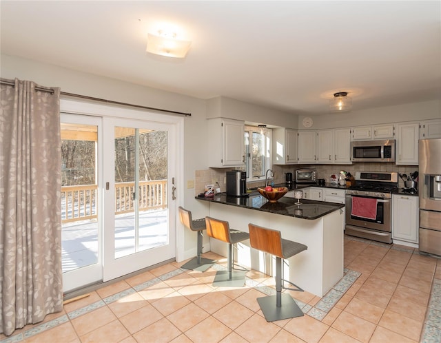 kitchen featuring white cabinets, backsplash, kitchen peninsula, and stainless steel appliances