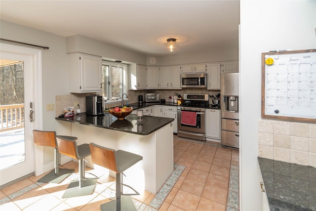 kitchen featuring stainless steel appliances, light tile patterned floors, kitchen peninsula, decorative backsplash, and white cabinets