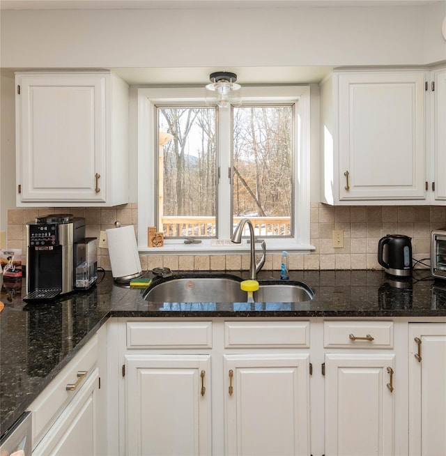 kitchen featuring tasteful backsplash, white cabinetry, dark stone countertops, and sink