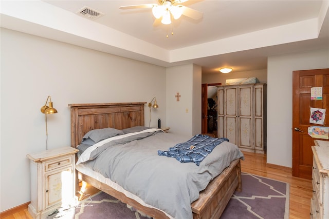 bedroom with light wood-type flooring, a raised ceiling, and ceiling fan