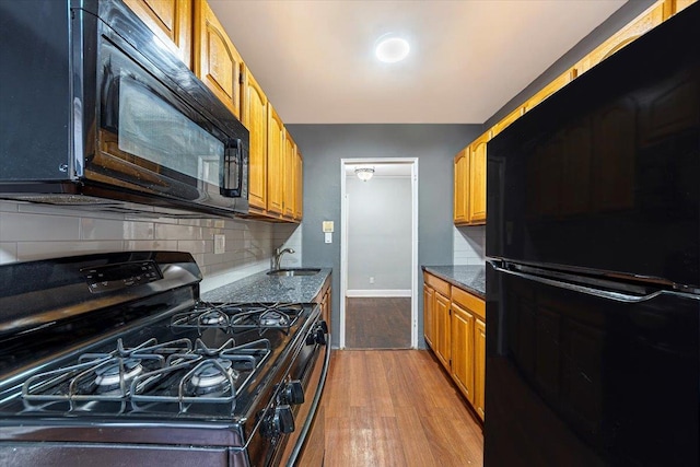 kitchen featuring wood-type flooring, black appliances, dark stone counters, sink, and backsplash