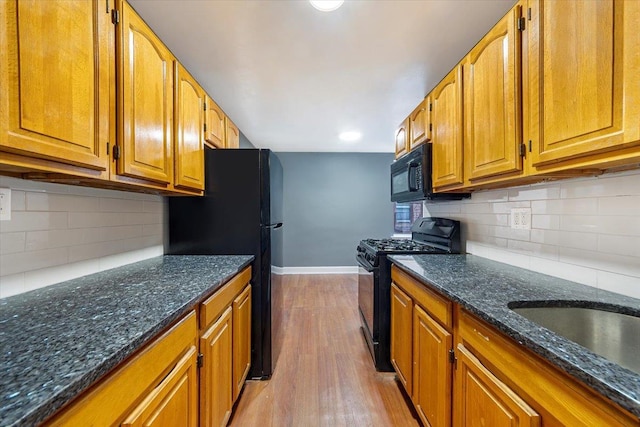 kitchen with light wood-type flooring, black appliances, decorative backsplash, and dark stone counters