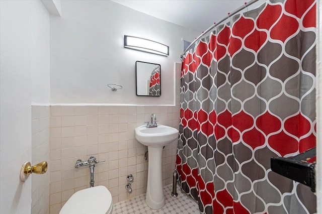 bathroom with tile walls, toilet, a shower with shower curtain, and sink