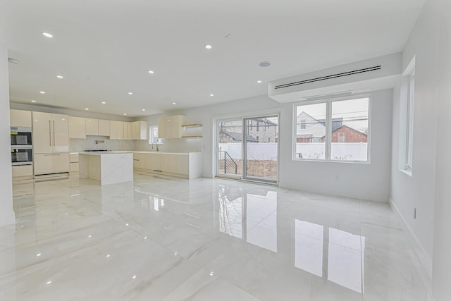 kitchen with white cabinetry, appliances with stainless steel finishes, decorative backsplash, a kitchen island, and light stone counters