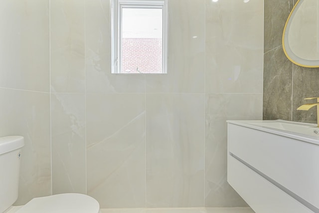 bathroom with toilet, vanity, and tile walls