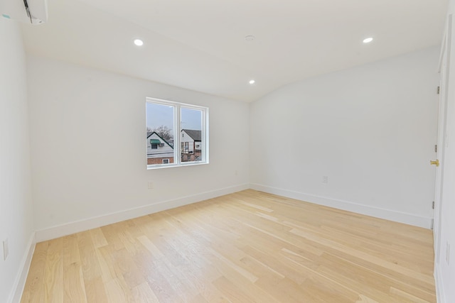 unfurnished room with a wall unit AC and light hardwood / wood-style flooring