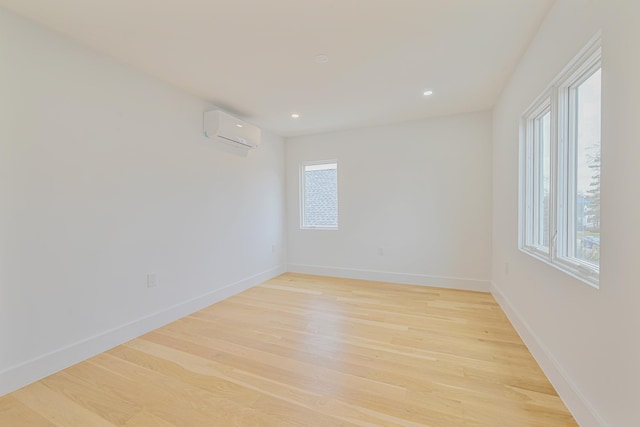 spare room with plenty of natural light, a wall unit AC, and light wood-type flooring