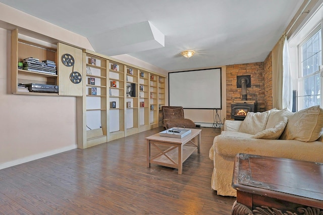 home theater featuring dark wood-type flooring, a wood stove, built in shelves, and baseboard heating