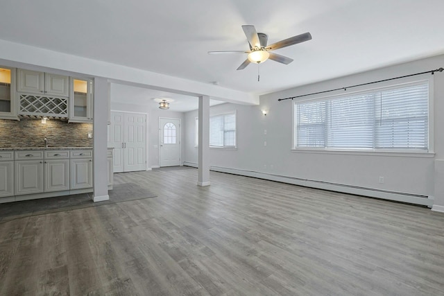 unfurnished living room featuring light wood-type flooring, ceiling fan, baseboard heating, and plenty of natural light