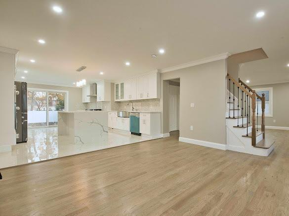 kitchen with white cabinetry, wall chimney exhaust hood, hanging light fixtures, crown molding, and light wood-type flooring