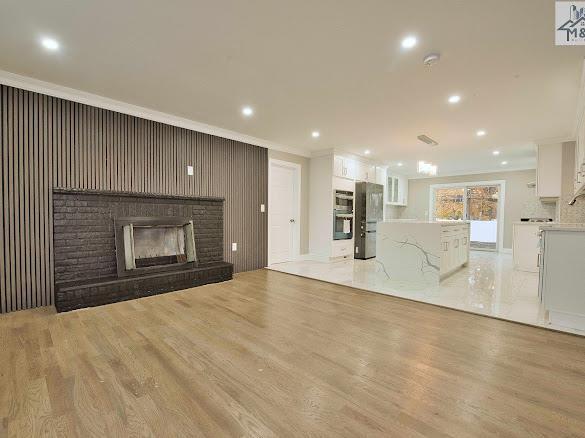 unfurnished living room featuring crown molding, light wood-type flooring, and a brick fireplace