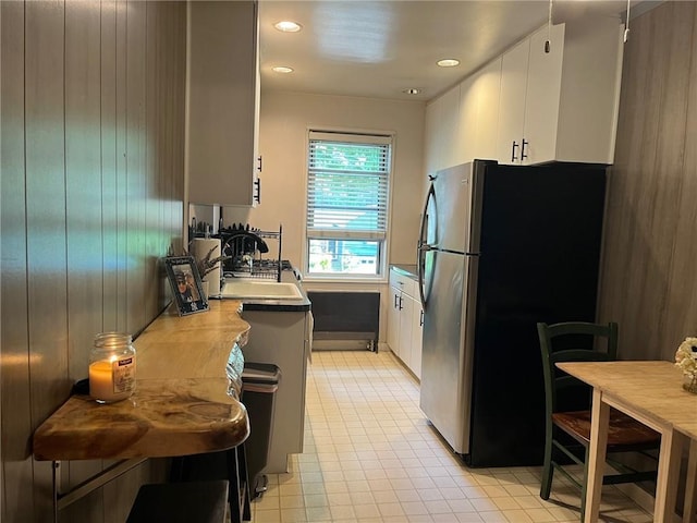 kitchen with white cabinets, sink, wooden walls, kitchen peninsula, and stainless steel refrigerator