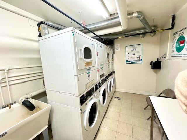 common laundry area with light tile patterned floors, baseboards, stacked washer and clothes dryer, independent washer and dryer, and a sink