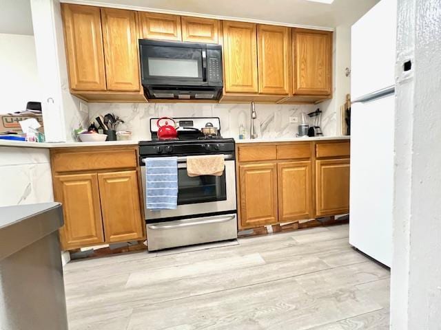 kitchen featuring black microwave, tasteful backsplash, stainless steel gas range, and light wood finished floors