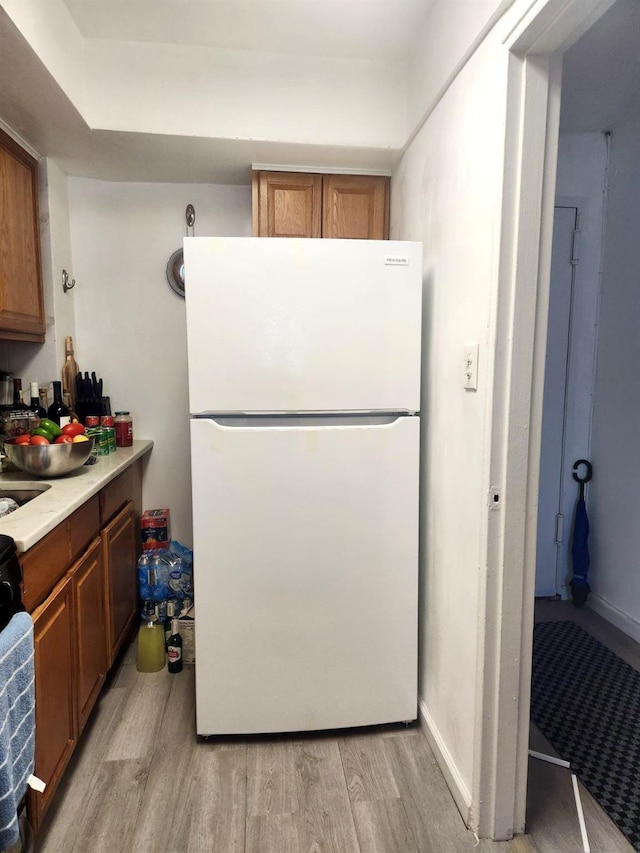 kitchen featuring light countertops, brown cabinetry, light wood-type flooring, and freestanding refrigerator