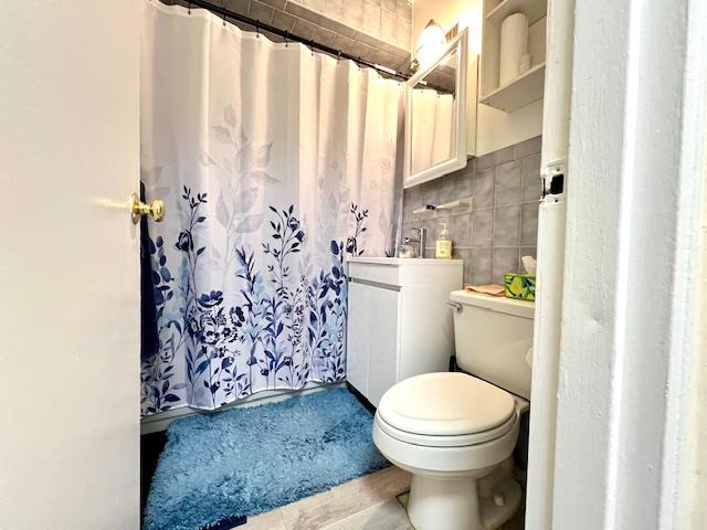 full bath featuring toilet, a shower with shower curtain, and tile walls