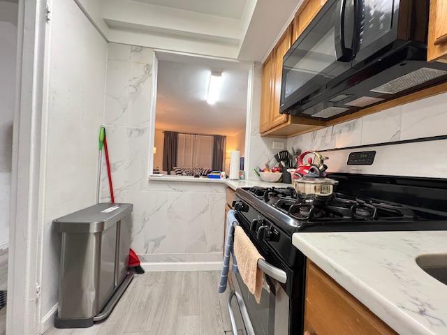 kitchen with brown cabinets, black microwave, light countertops, and stainless steel range with gas stovetop