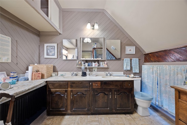 bathroom with vanity, toilet, vaulted ceiling, and wood walls