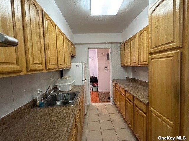 kitchen featuring light tile patterned flooring, white refrigerator, and sink