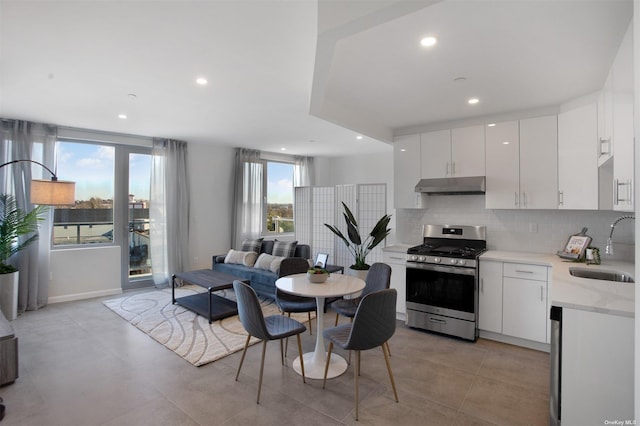 kitchen with backsplash, stainless steel gas range oven, white cabinetry, and sink