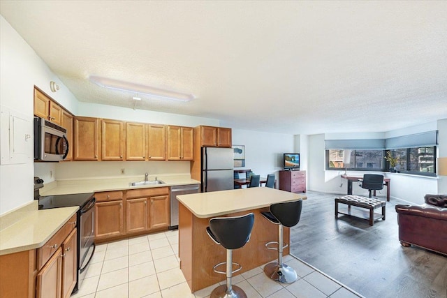 kitchen featuring sink, a center island, stainless steel appliances, a textured ceiling, and a kitchen bar