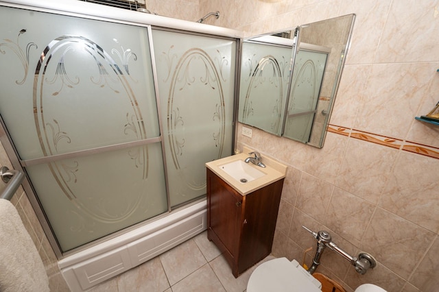 full bathroom with tile patterned floors, bath / shower combo with glass door, toilet, vanity, and tile walls