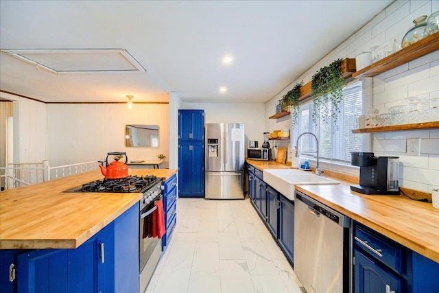 kitchen featuring tasteful backsplash, stainless steel appliances, sink, blue cabinetry, and butcher block counters