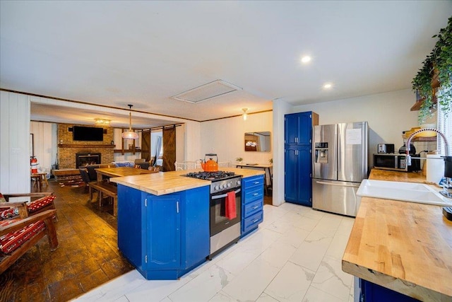 kitchen with stainless steel appliances, blue cabinets, sink, a fireplace, and butcher block countertops