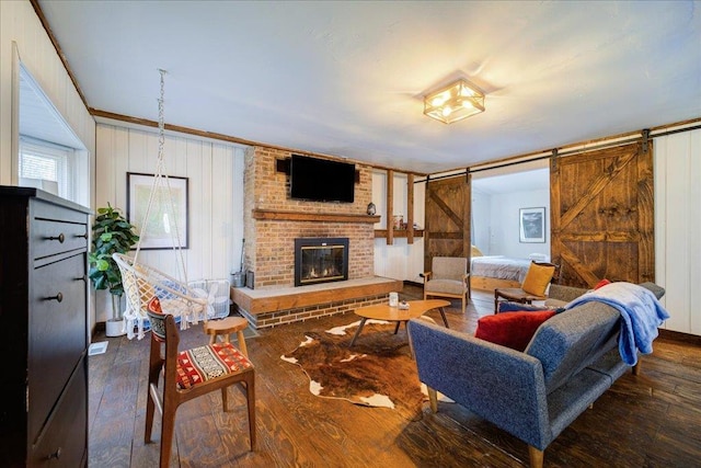 living room with a barn door, a brick fireplace, and dark wood-type flooring