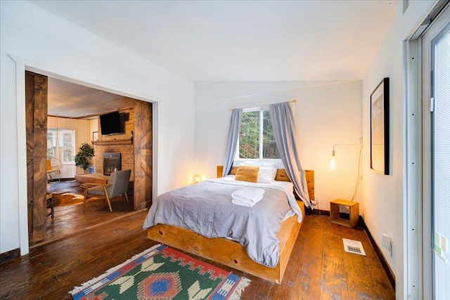 bedroom with lofted ceiling, dark hardwood / wood-style floors, and a brick fireplace