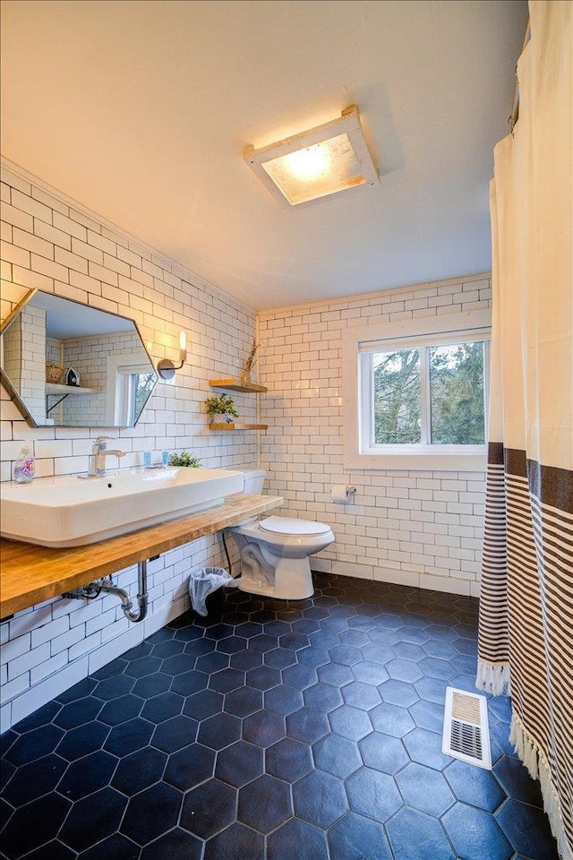 bathroom featuring brick wall, toilet, and sink