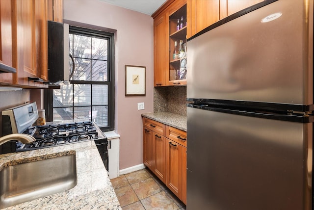 kitchen featuring sink, decorative backsplash, white gas range, light stone countertops, and stainless steel refrigerator