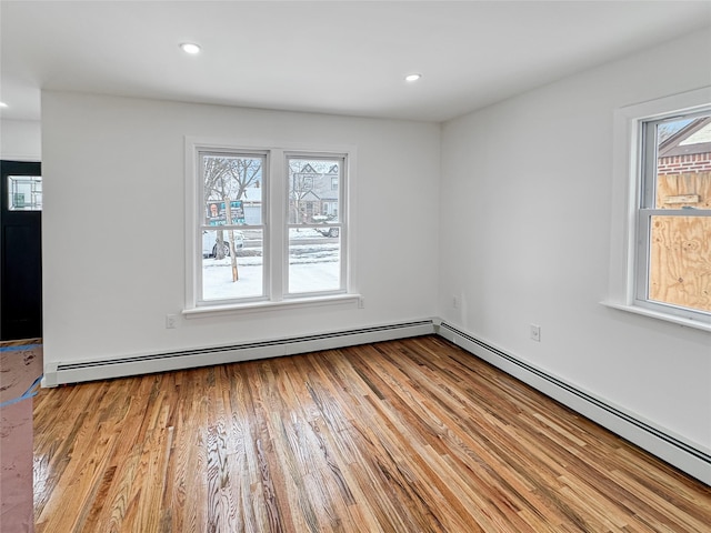 empty room featuring a healthy amount of sunlight, light wood-type flooring, and a baseboard heating unit