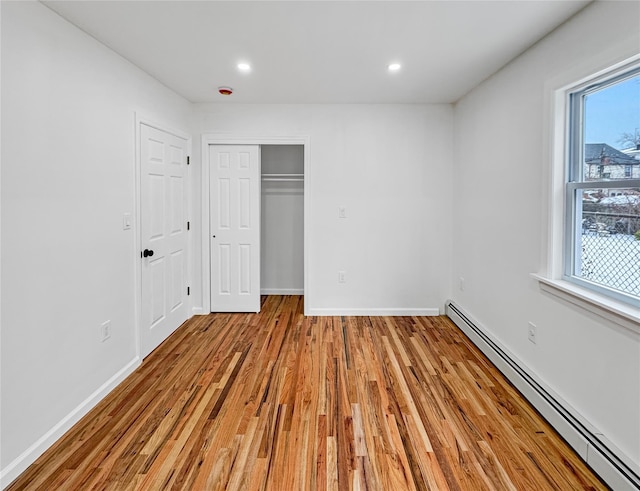 unfurnished bedroom featuring a baseboard radiator, a closet, and light wood-type flooring