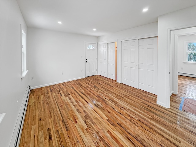 unfurnished bedroom featuring multiple closets, light hardwood / wood-style flooring, and a baseboard heating unit