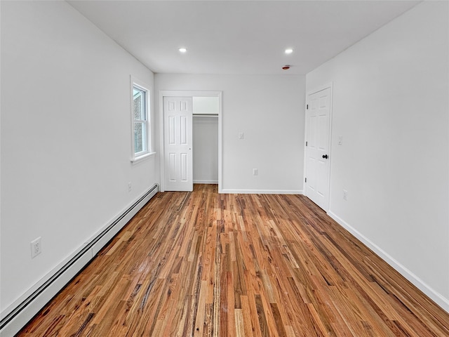 unfurnished bedroom featuring a closet, baseboard heating, and light hardwood / wood-style floors