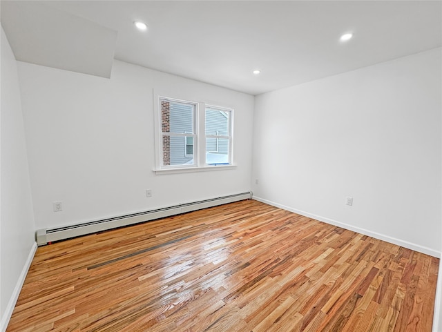 unfurnished room featuring a baseboard heating unit and light wood-type flooring