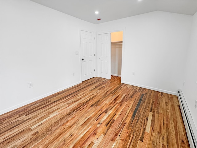 unfurnished bedroom with a baseboard radiator, vaulted ceiling, a closet, and light wood-type flooring