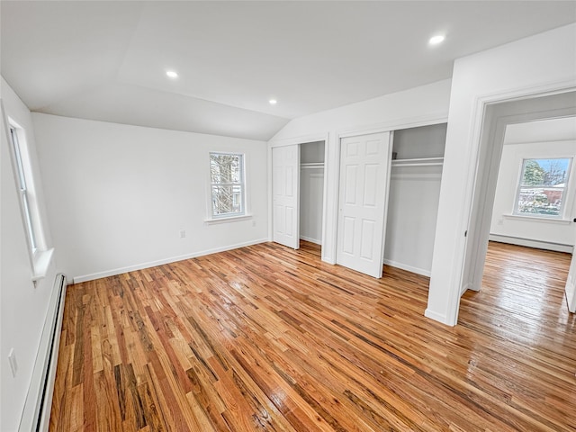 unfurnished bedroom featuring multiple windows, two closets, light wood-type flooring, and baseboard heating