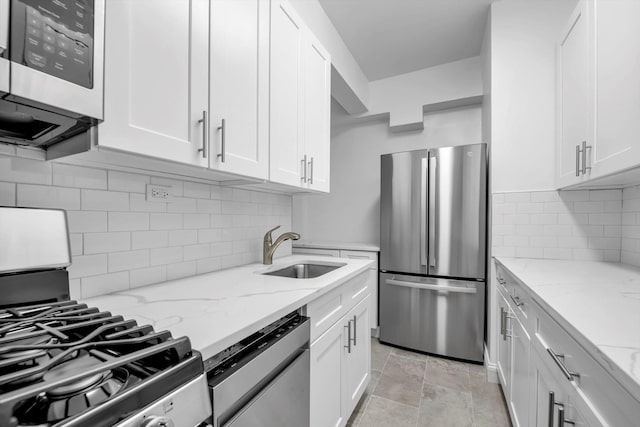 kitchen featuring white cabinets, appliances with stainless steel finishes, light stone countertops, and sink