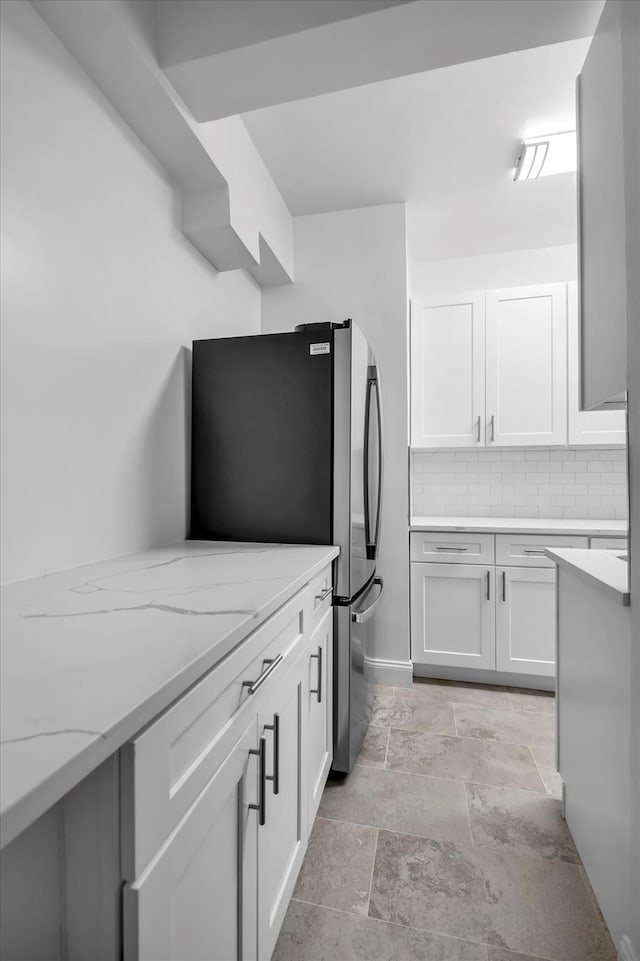 kitchen featuring stainless steel fridge, light stone countertops, white cabinetry, and tasteful backsplash