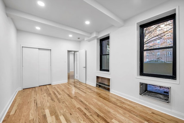 unfurnished bedroom with beam ceiling and light wood-type flooring