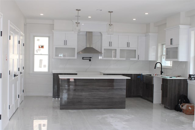 kitchen featuring backsplash, wall chimney exhaust hood, decorative light fixtures, white cabinetry, and a kitchen island