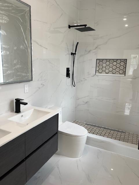 bathroom with a tile shower, vanity, toilet, and tile walls