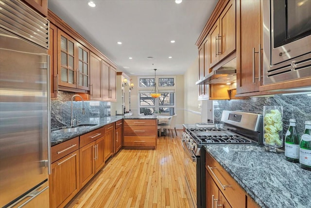 kitchen featuring sink, dark stone countertops, hanging light fixtures, stainless steel appliances, and light hardwood / wood-style floors