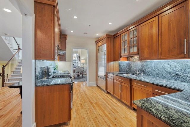 kitchen featuring sink, appliances with stainless steel finishes, dark stone countertops, decorative backsplash, and light wood-type flooring