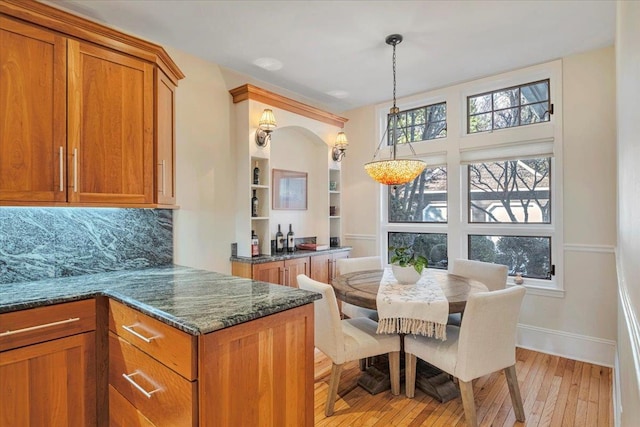 kitchen with decorative backsplash, built in shelves, decorative light fixtures, dark stone counters, and light wood-type flooring