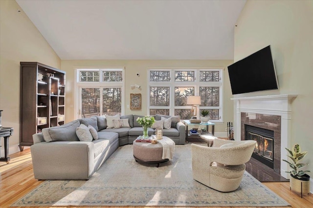 living room with high vaulted ceiling, light hardwood / wood-style floors, and a premium fireplace