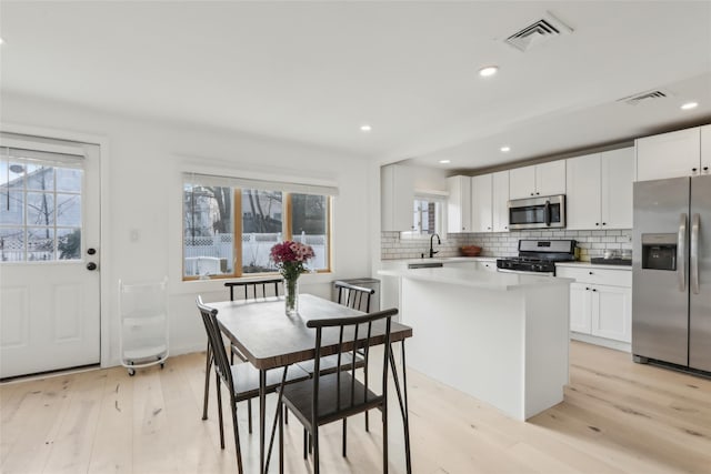 kitchen featuring sink, light hardwood / wood-style flooring, a kitchen island, white cabinetry, and stainless steel appliances