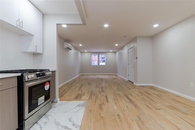 kitchen with a wall mounted AC, stainless steel range, white cabinets, and light hardwood / wood-style flooring